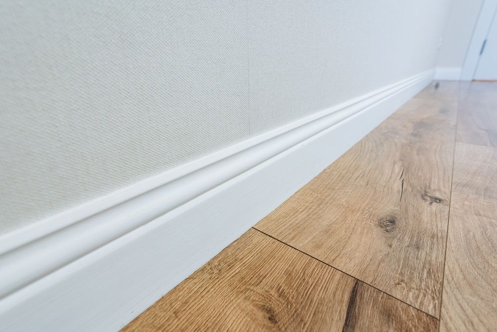 Close-up of white baseboard along a textured wall beside light wood flooring