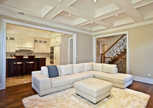 Bright living room with white sectional sofa, tray ceiling, and open view to kitchen and staircase