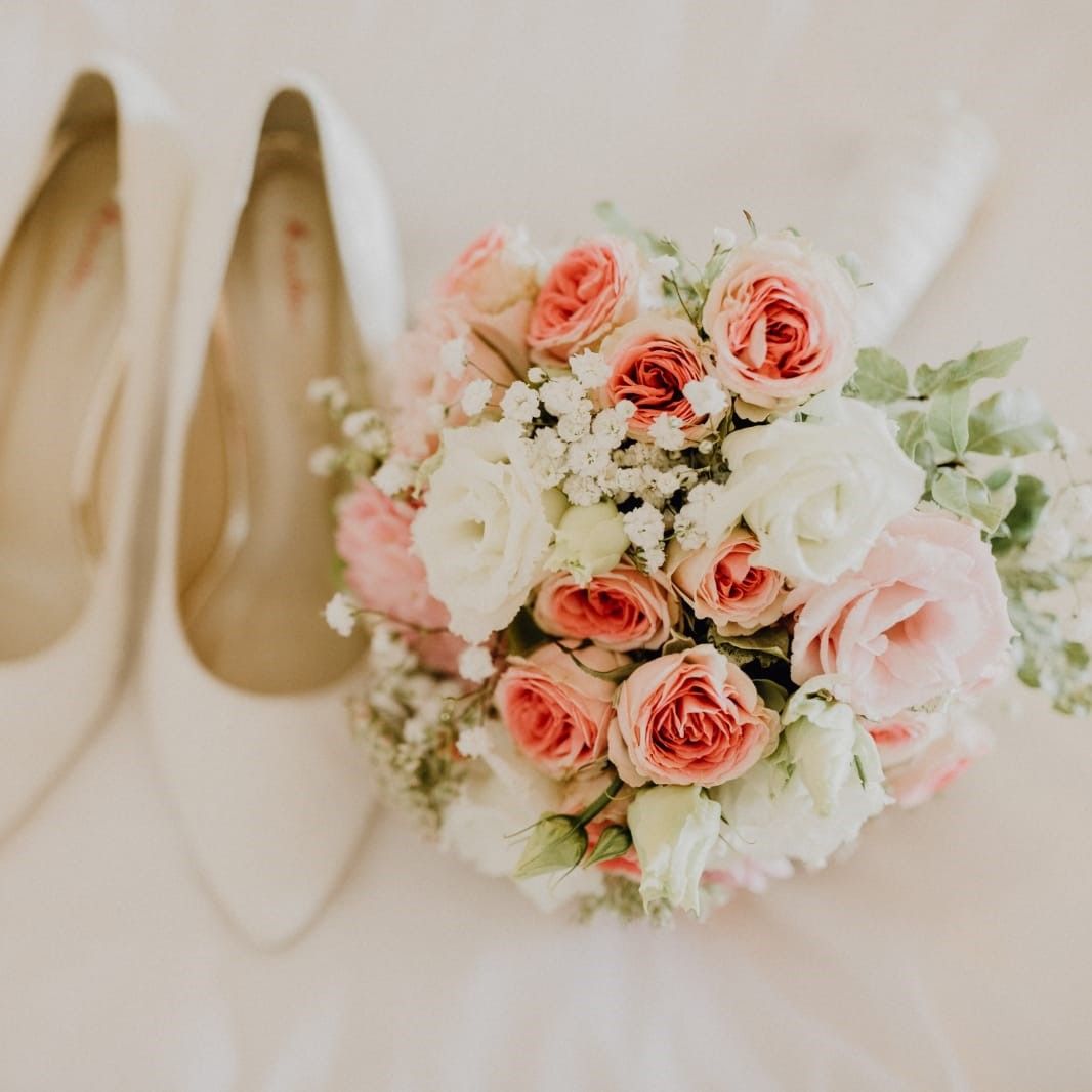 ein Blumenstrauß und ein Paar Hochzeitsschuhe liegen auf einem Bett .