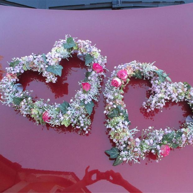 zwei Herzen aus Blumenkranz auf der Motorhaube eines Autos