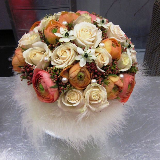 ein Blumenstrauß aus rosa und weißen Rosen sitzt auf einem weißen Pelzkissen