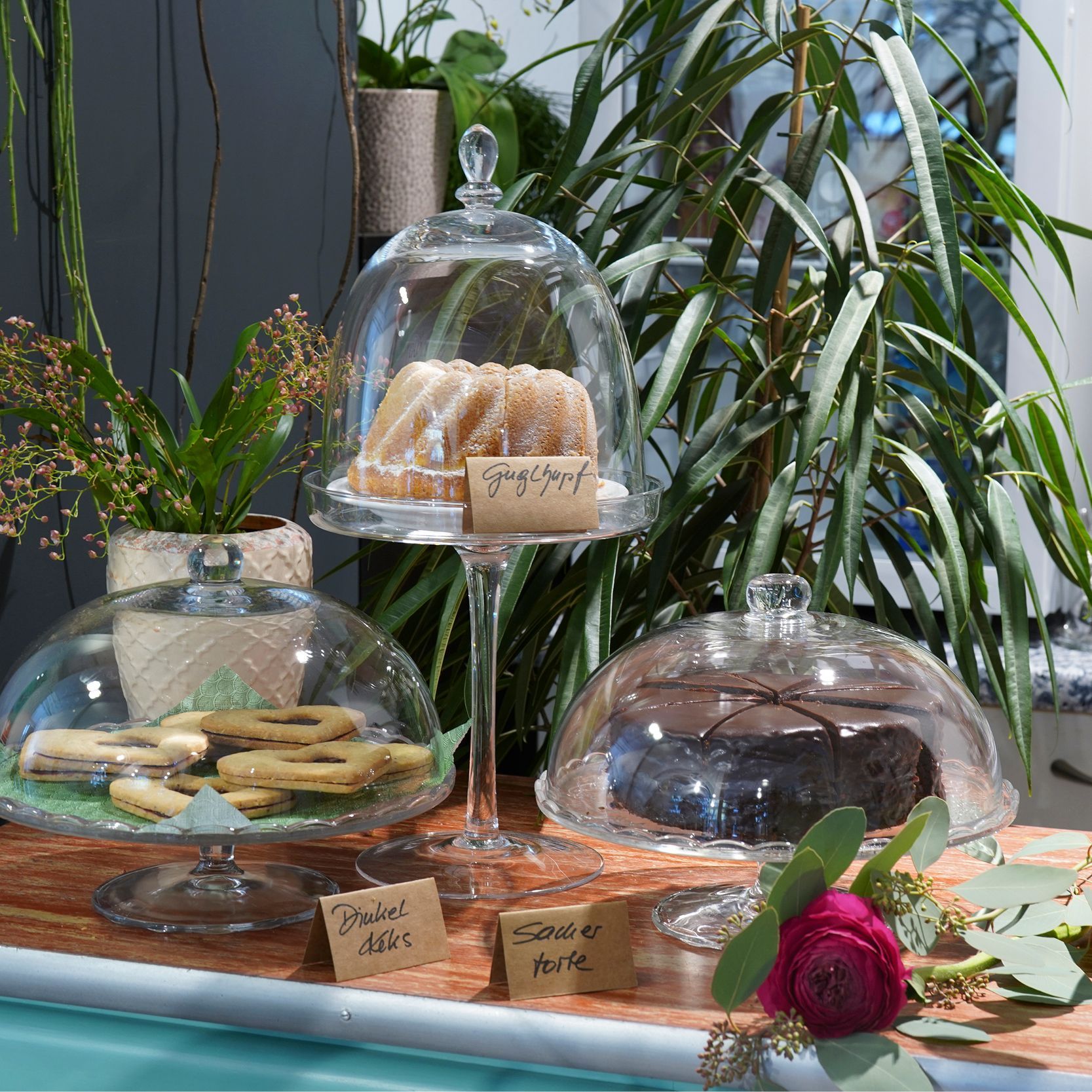 Auf einem Tisch stehen drei Glasglocken mit Kuchen darauf .