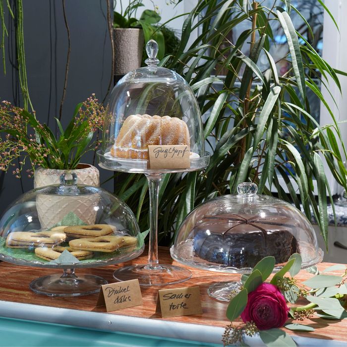 Auf einem Tisch stehen drei Glasglocken mit Kuchen darauf .