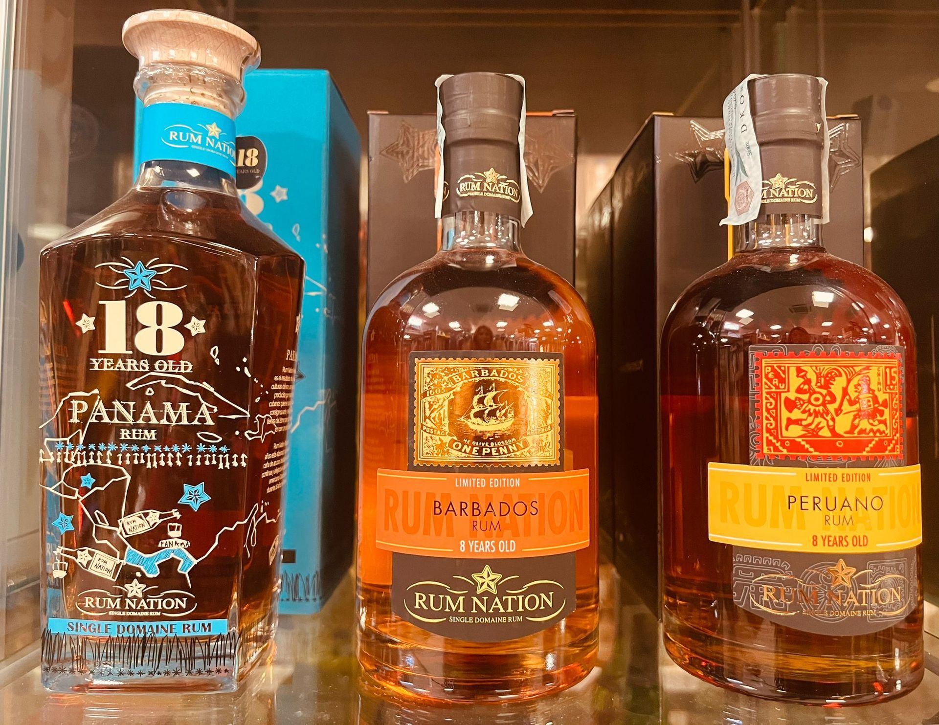 Tre bottiglie di vetro di liquori Rum Nation esposte su uno scaffale, con un rum Panama invecchiato 18 anni in bella vista.