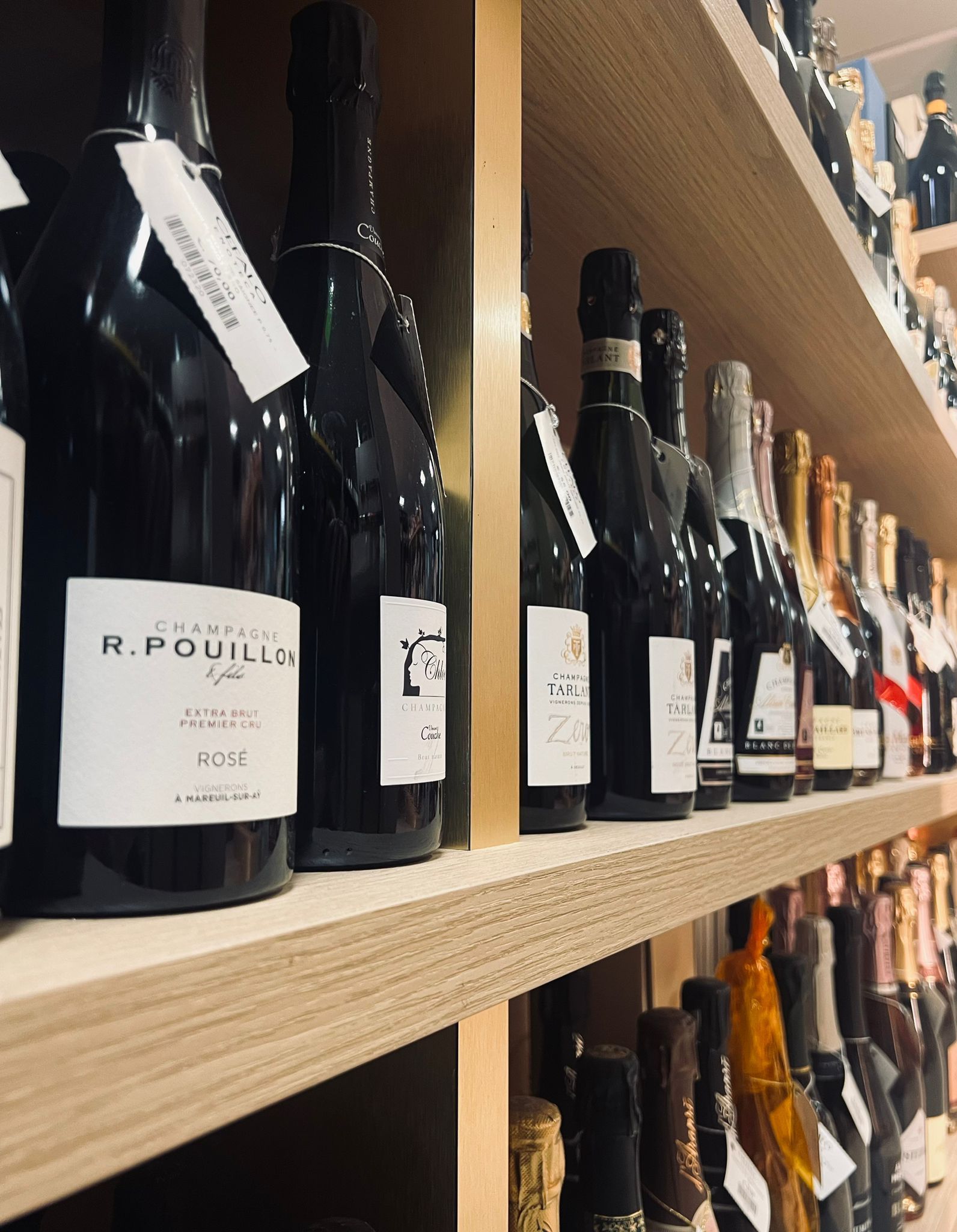 In un negozio, file di bottiglie di vino con etichette bianche sono allineate su scaffali di legno.