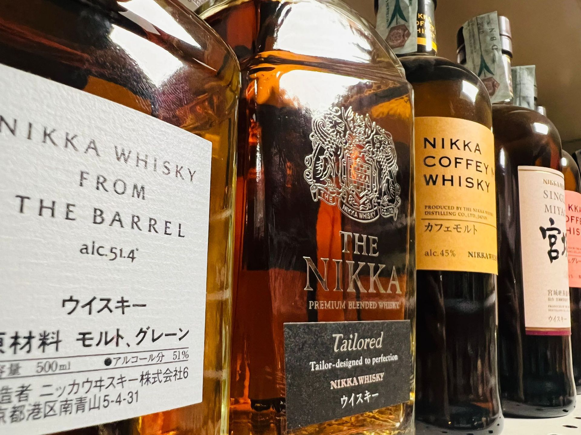 Una fila di diverse bottiglie di whisky Nikka su uno scaffale, con etichette come 