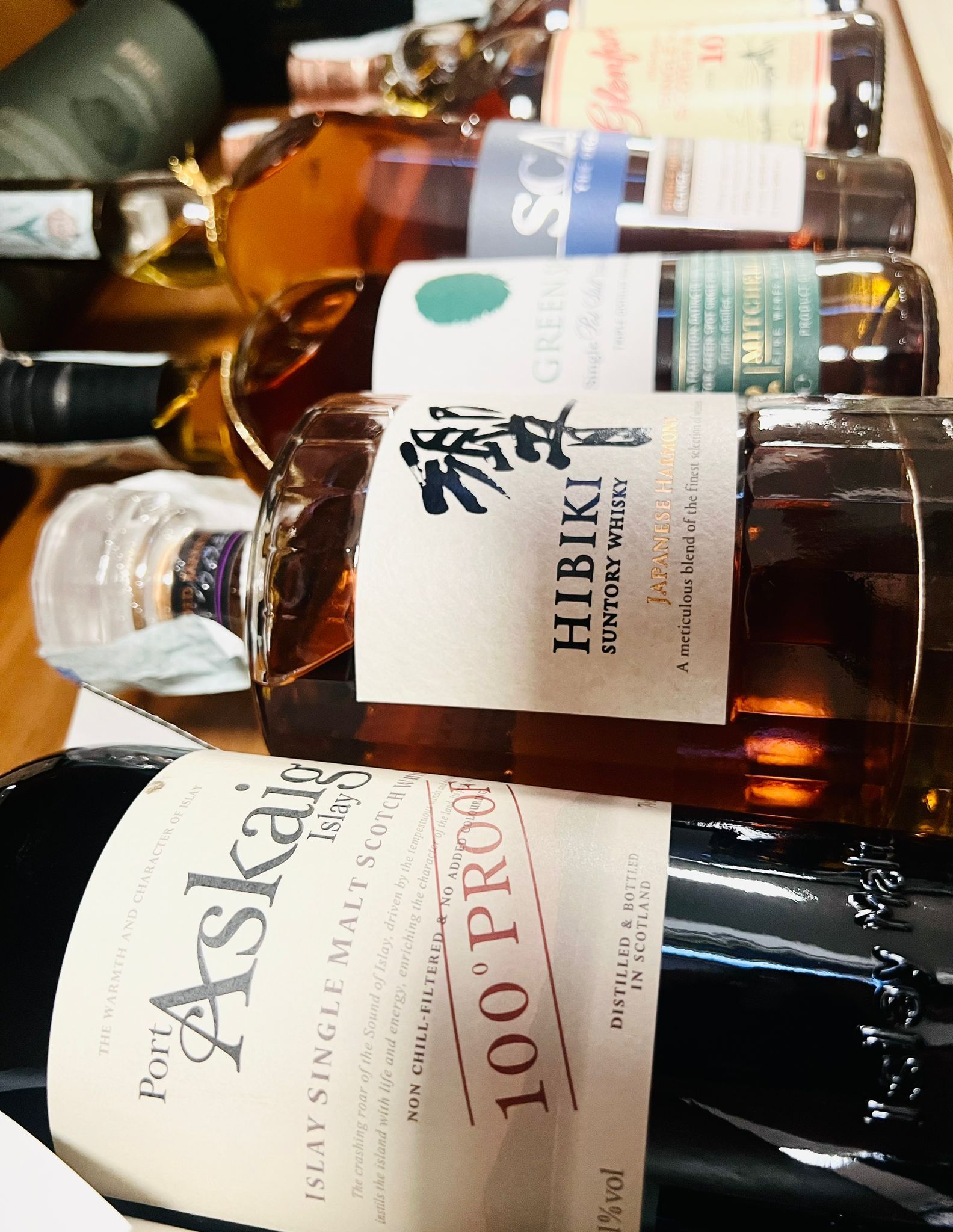 Un primo piano di una selezione di bottiglie di whisky disposte su uno scaffale, con etichette come Hibiki e Port Askaig.