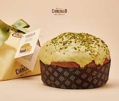 Un panettone glassato al pistacchio è esposto accanto alla sua confezione regalo e all'etichetta del prodotto su uno sfondo beige.