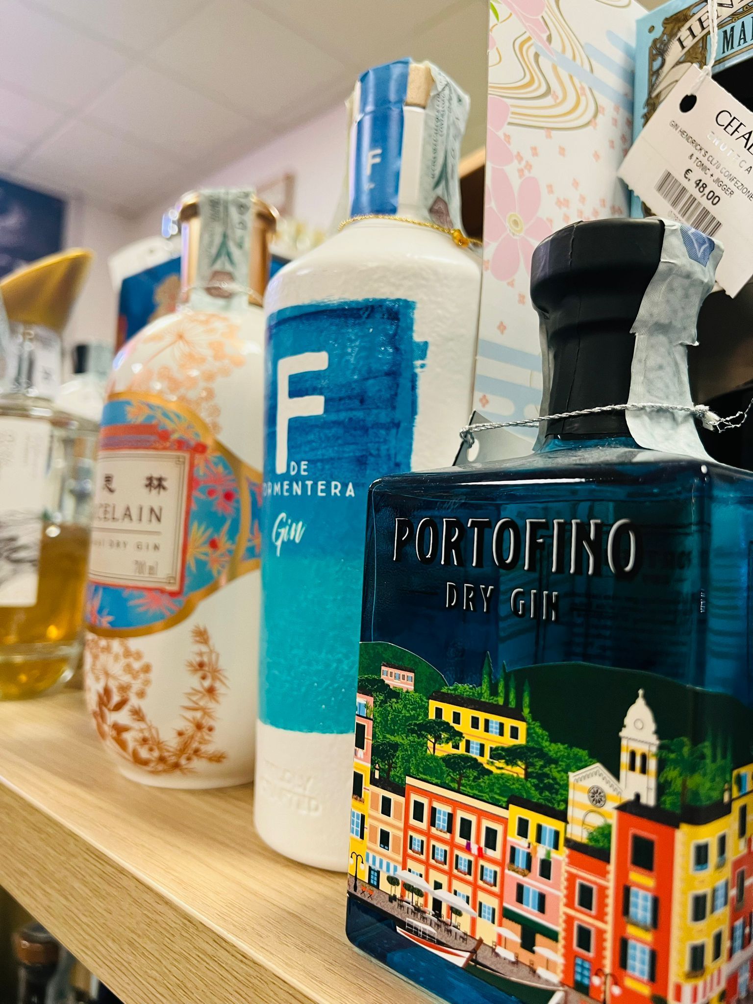 Un primo piano di tre bottiglie di gin allineate su uno scaffale di legno di un negozio, tra cui il Portofino Dry Gin in primo piano.