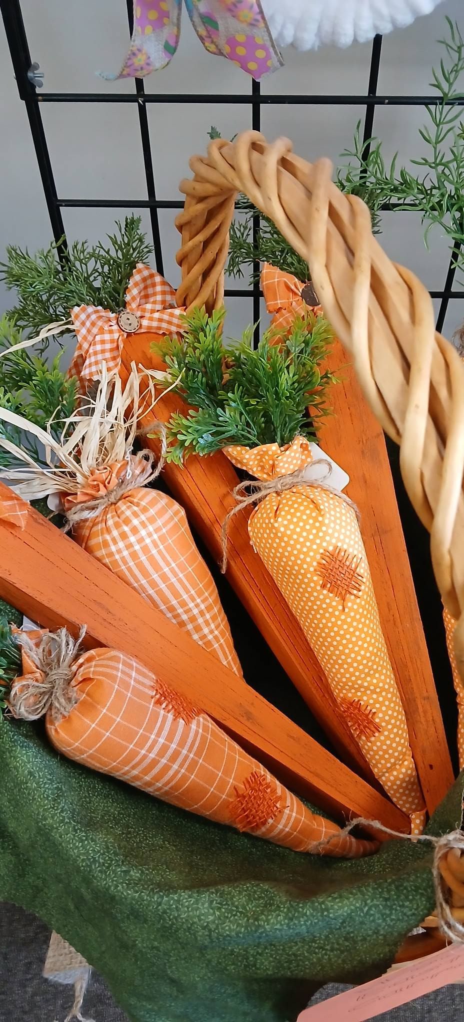 Orange woven carrot decorations in a basket with greenery and a braided handle against a black grid backdrop