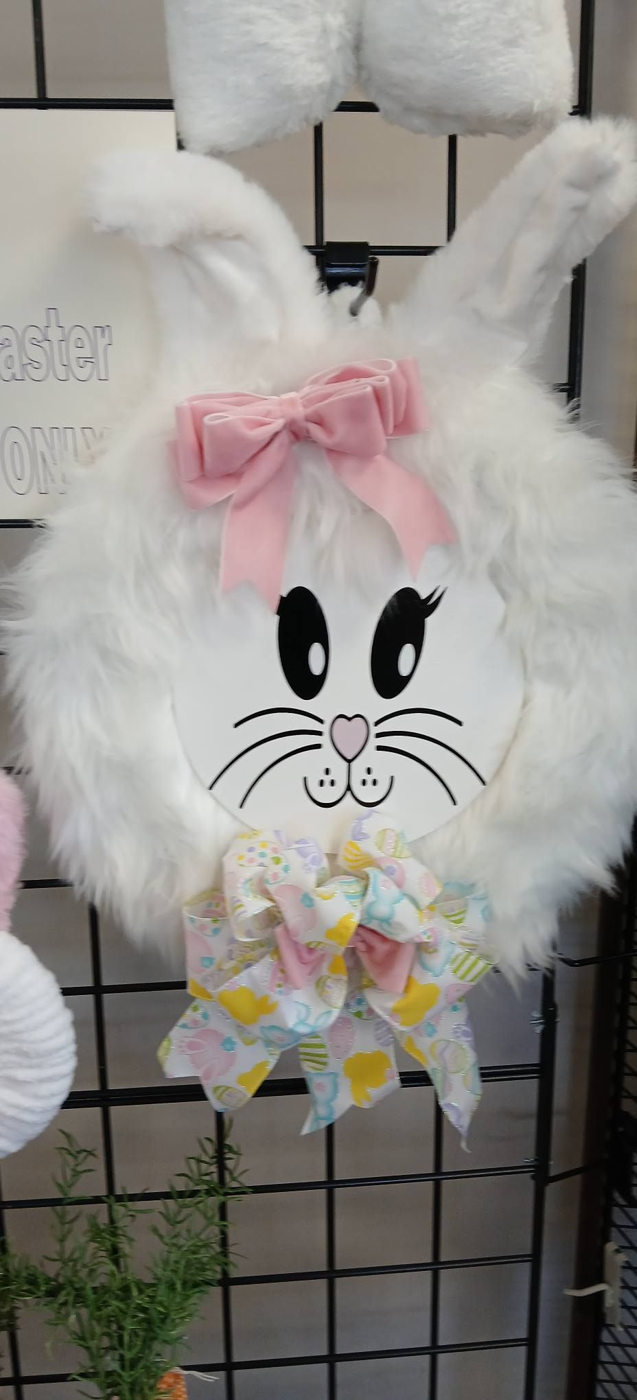 White plush bunny Easter decoration with pink bow and pastel floral ribbon on a wire grid display