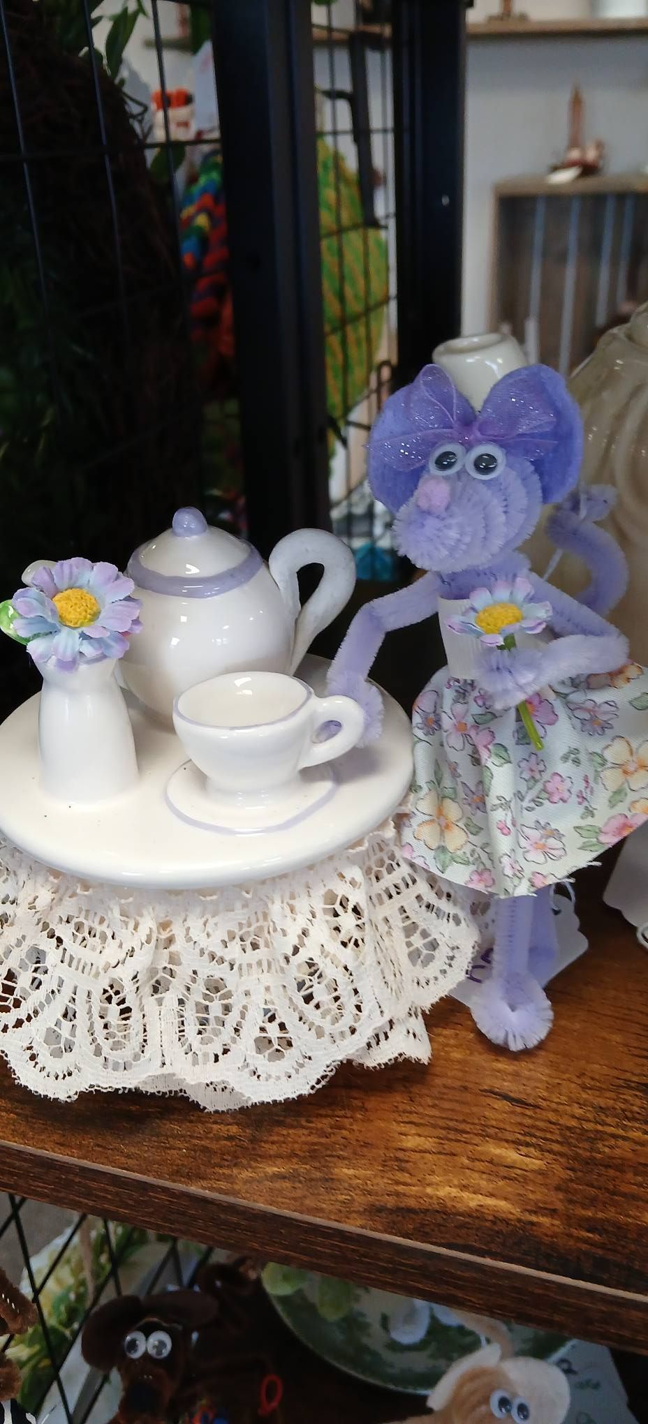 Purple stuffed cat beside a white tea set on a lace doily on a wooden shelf