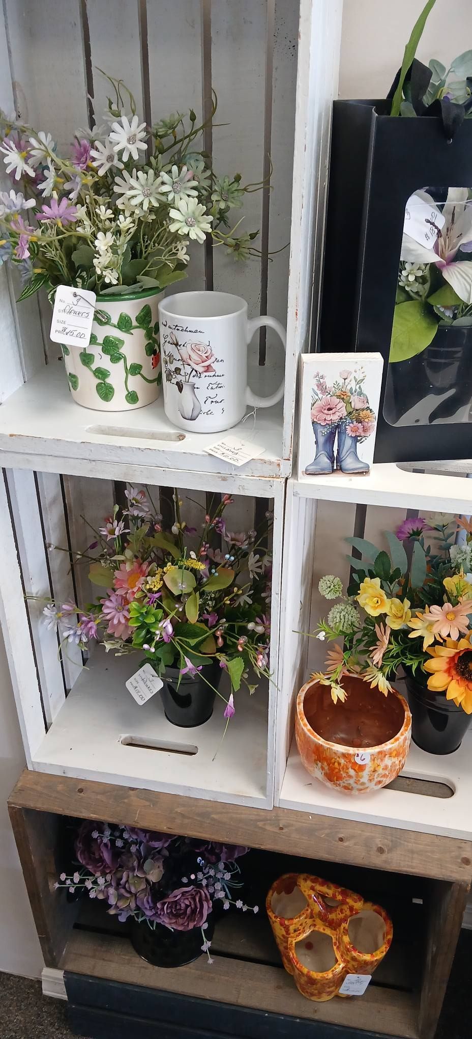 White display shelf with several small potted flowers and decorative plant arrangements.