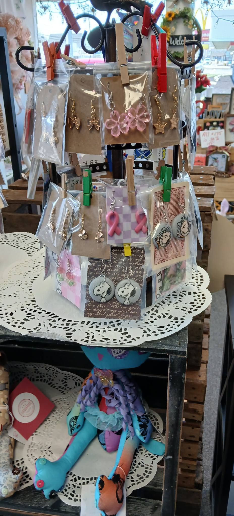 Display of pastel keychains and accessories on a rotating shop stand, with a stuffed doll below