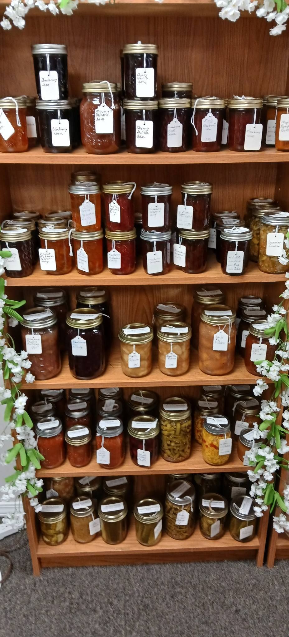 Wooden shelves filled with assorted jars of preserves and spices, decorated with white flowers