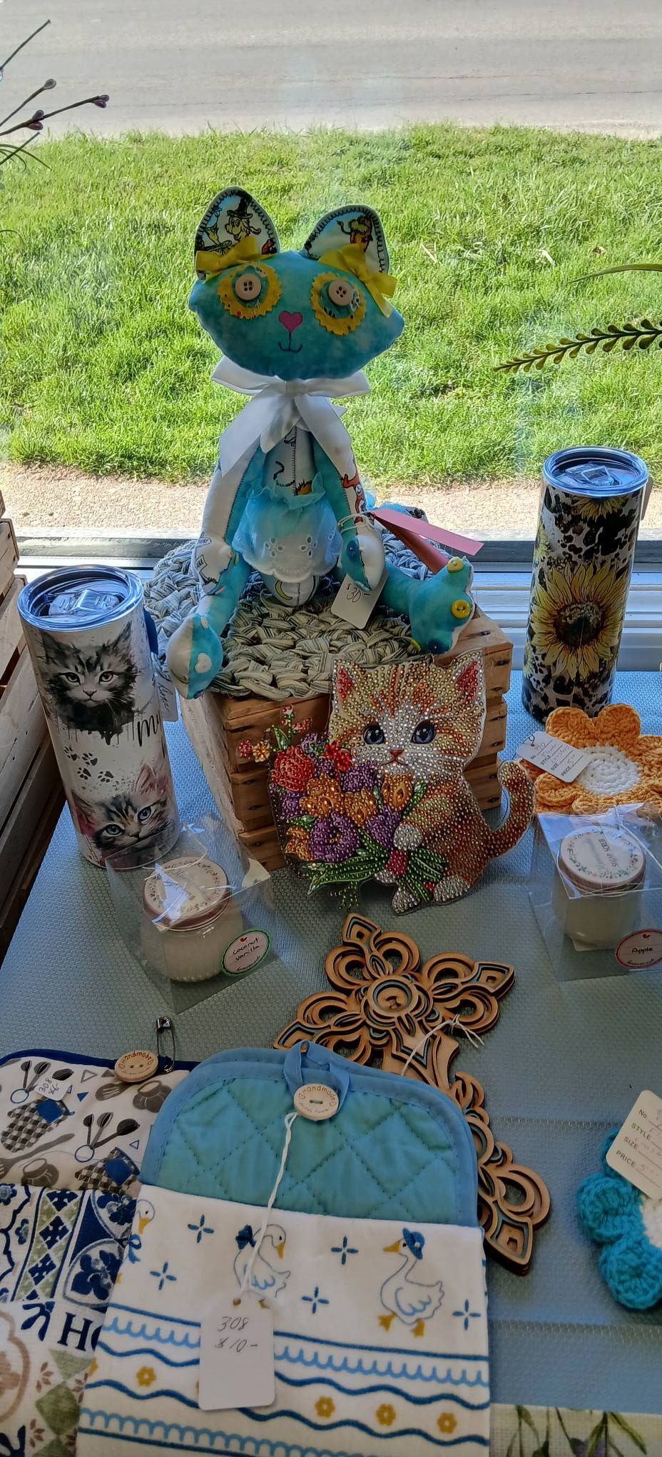 Colorful owl-themed craft display on a table, with painted bottles, beaded decorations, and a teal pouch outdoors