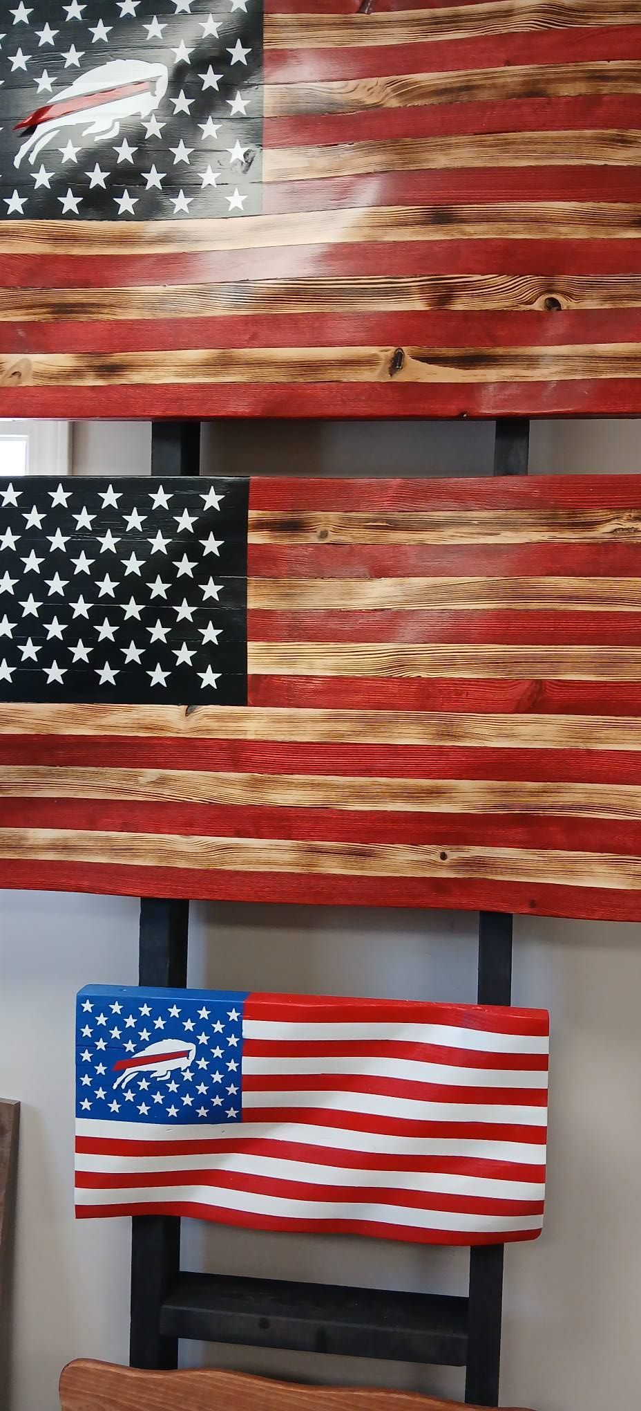 Three U.S. flags displayed indoors, with two larger worn flags above a smaller flag on a fireplace mantle