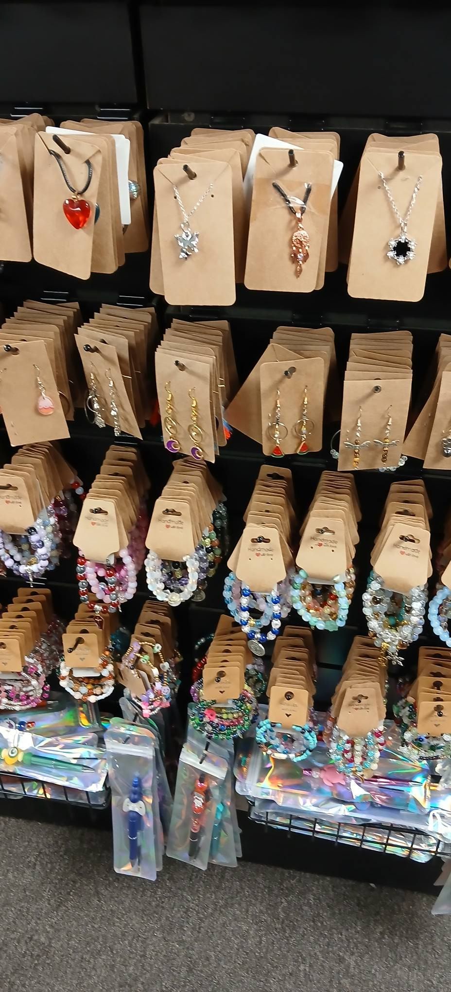 Hanging rows of small gift bags with tags on a store display rack, with colorful items on the bottom shelf