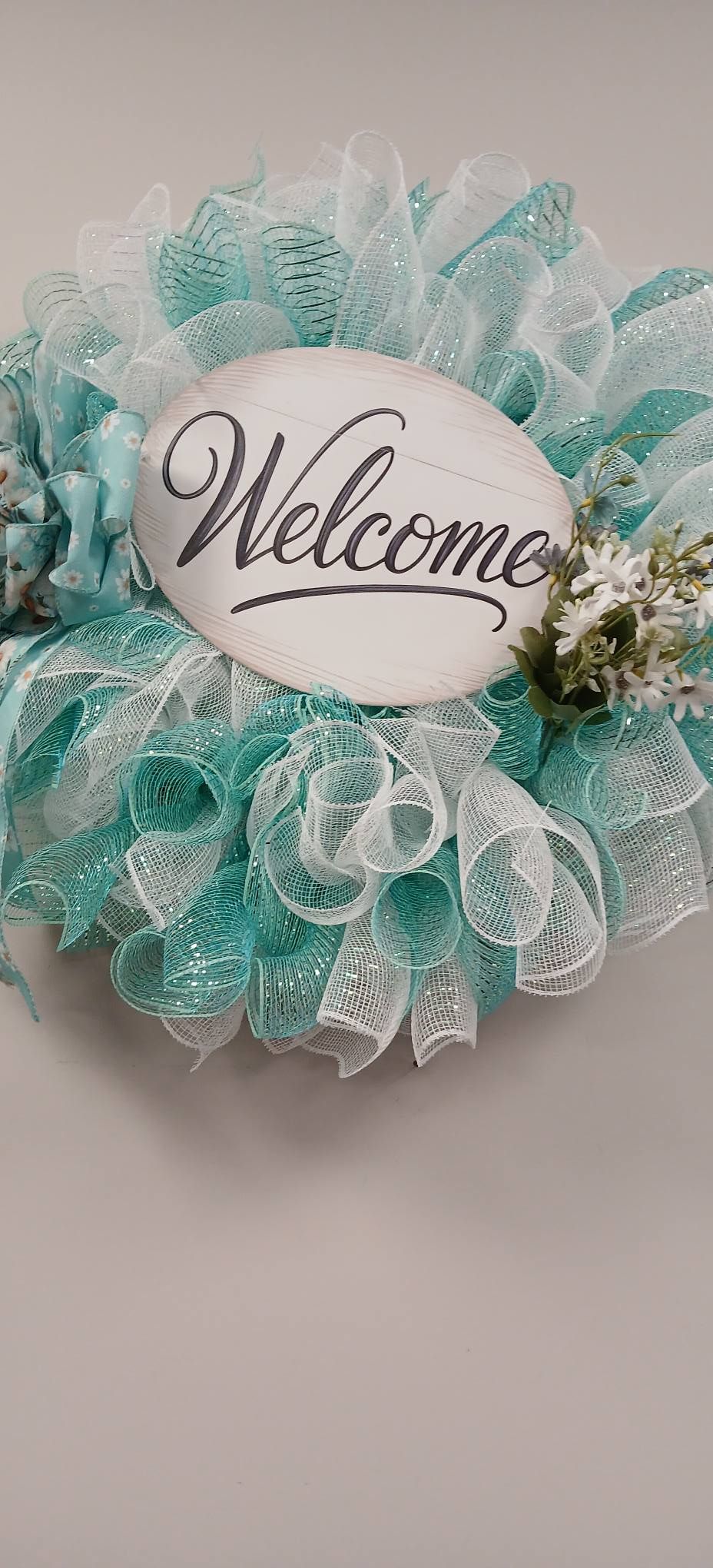 Turquoise and white decorative wreath with a “Welcome” sign and small floral accents