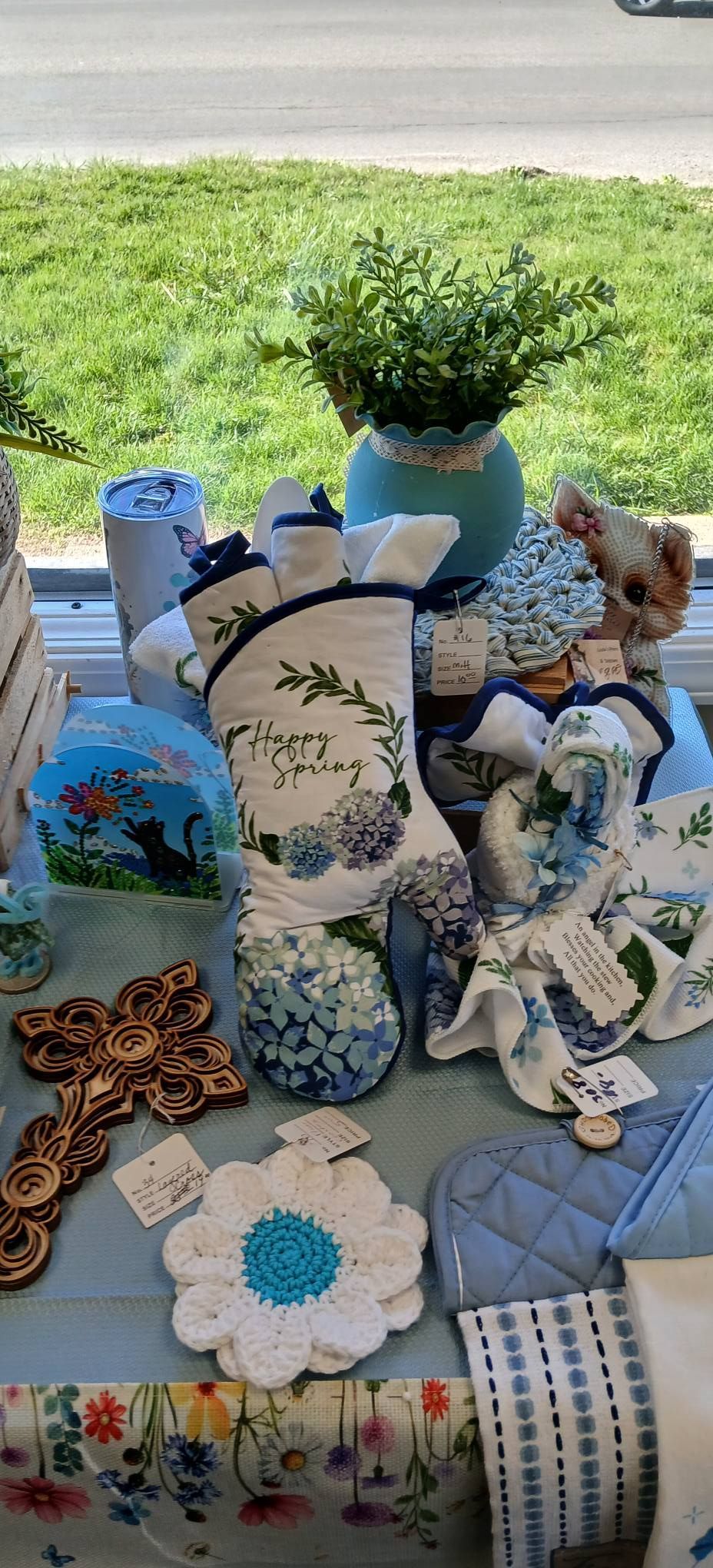 Decorative handmade crafts and blue-and-white painted items arranged on a table outdoors, with a potted plant behind them