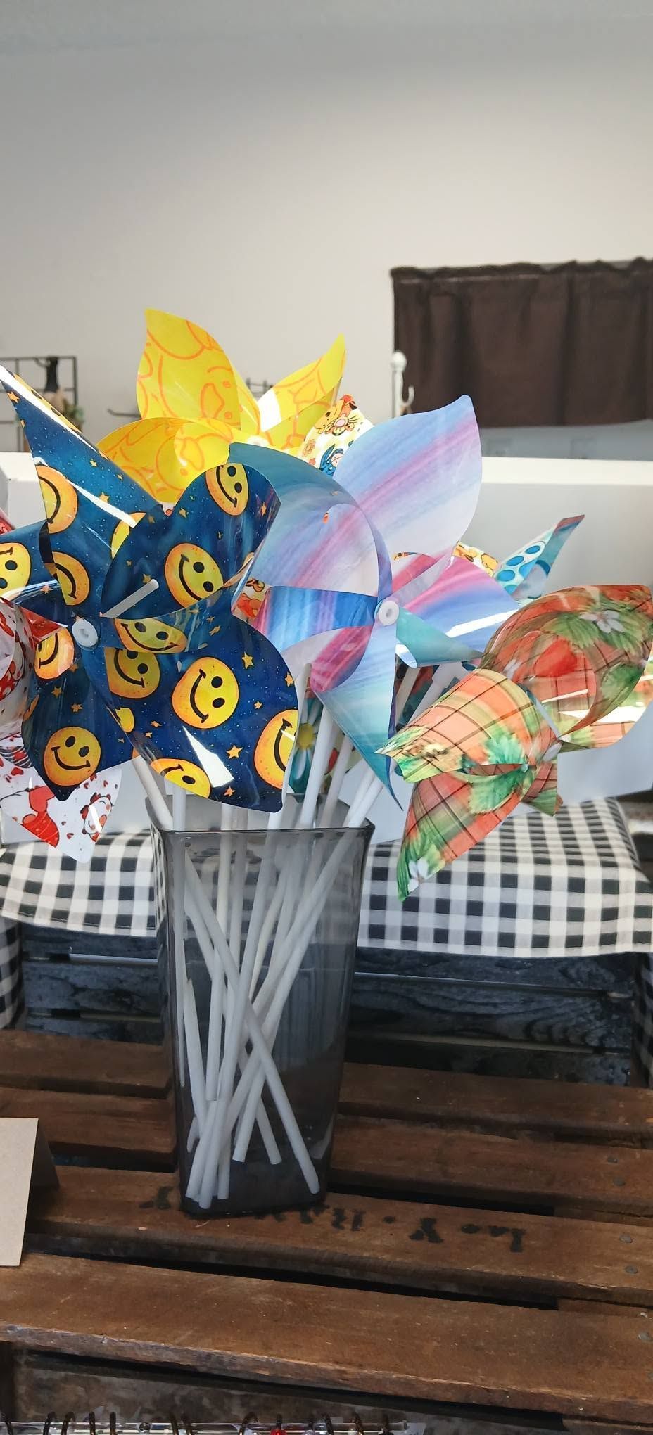Colorful wrapped lollipops in a vase on a wooden bench in front of a checkered tablecloth.