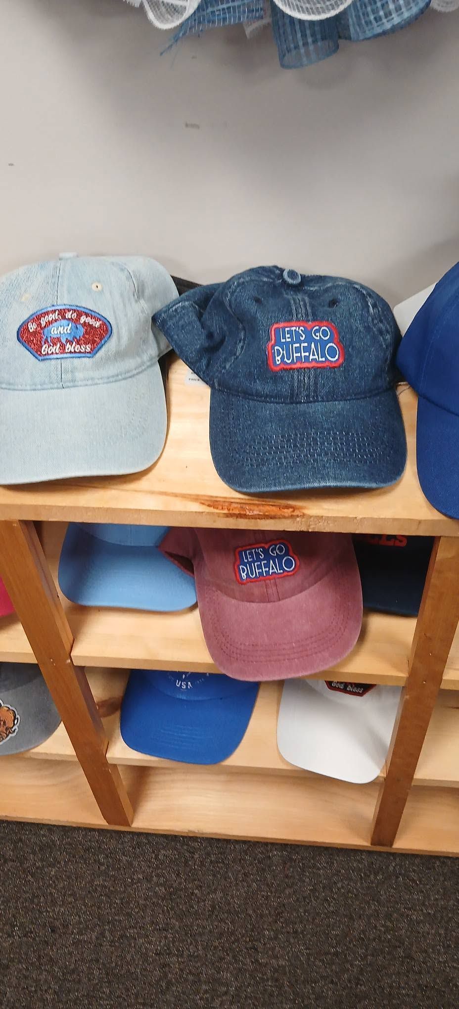 Five baseball caps in light blue, dark blue, red, and blue on a wooden shelf.
