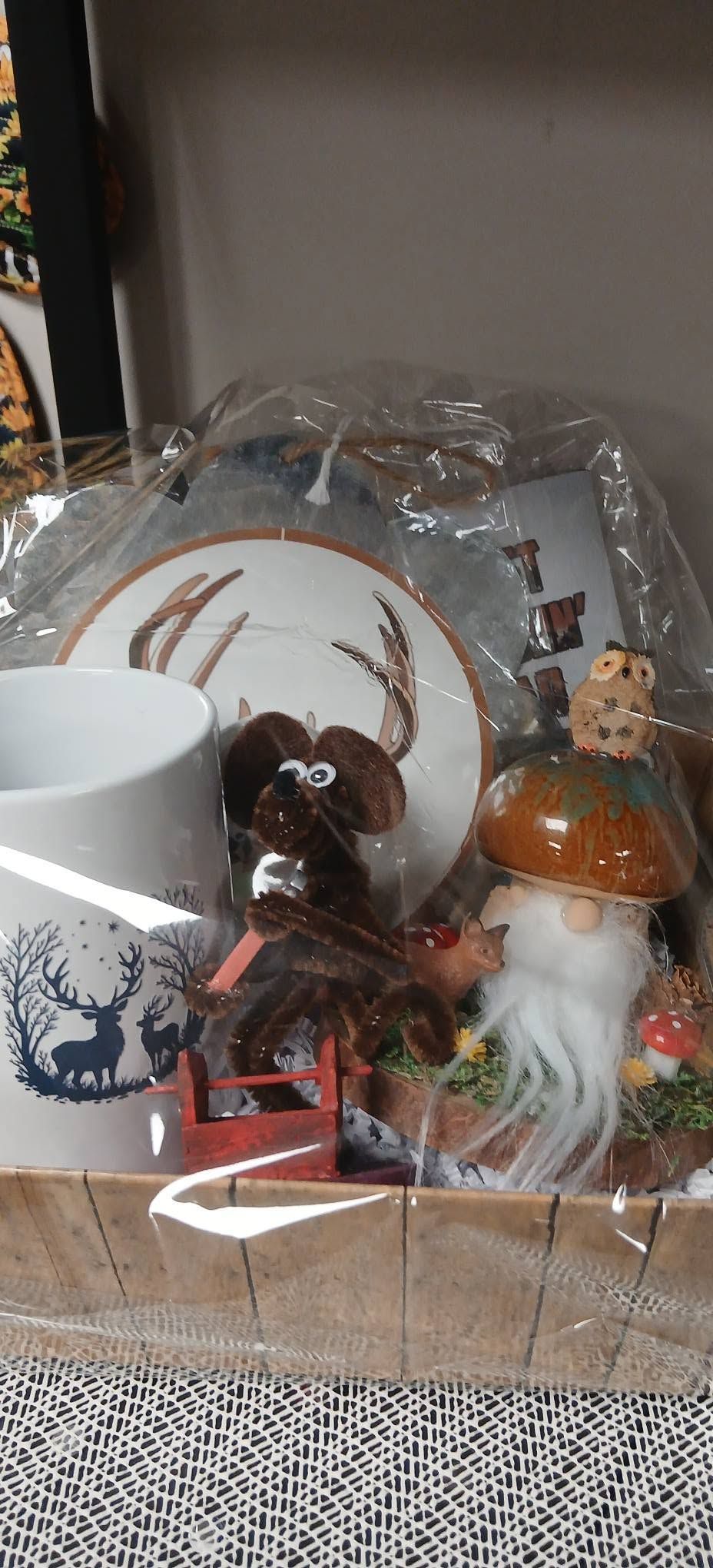 Gift basket with a white mug, decorative deer plates, and small holiday figurines in clear wrapping