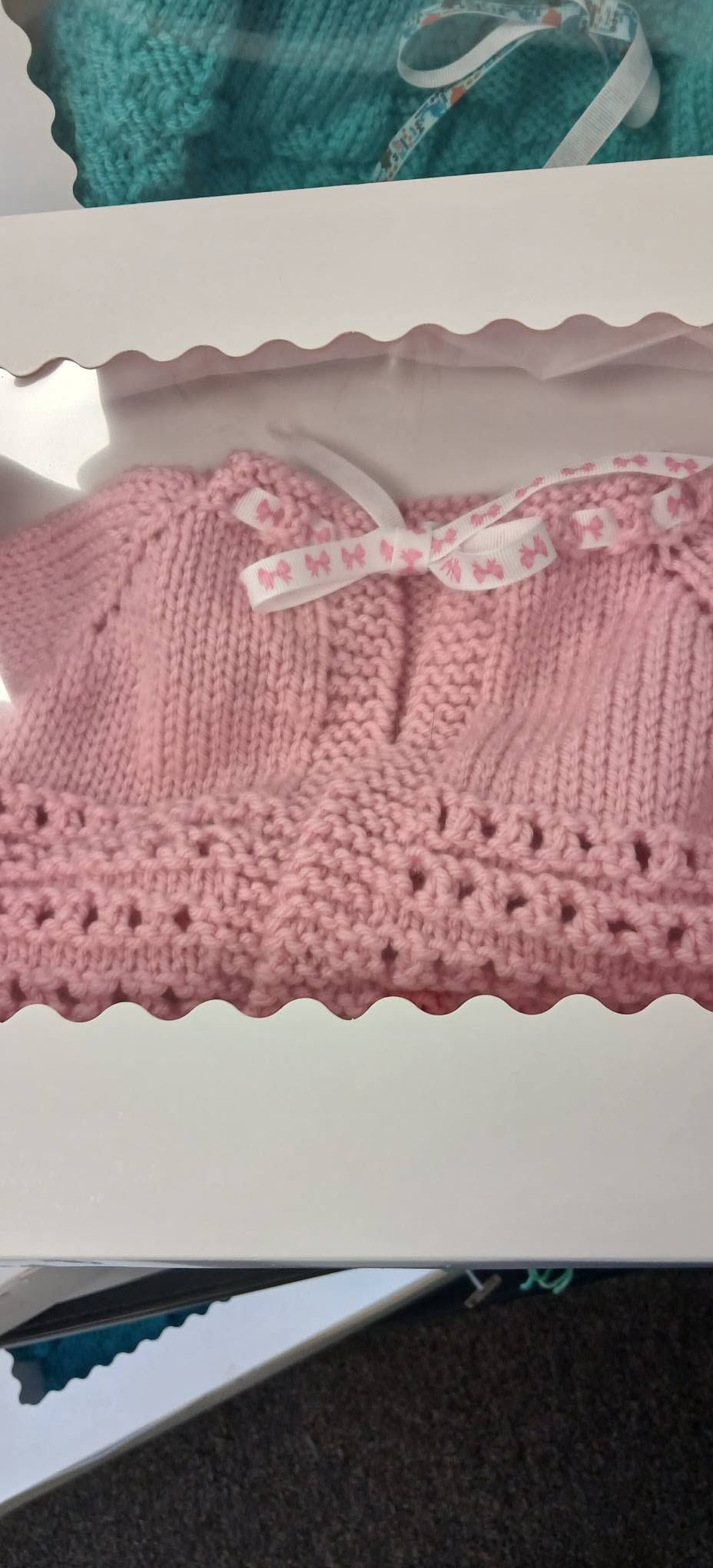 Pink knitted baby sweaters displayed in a white box