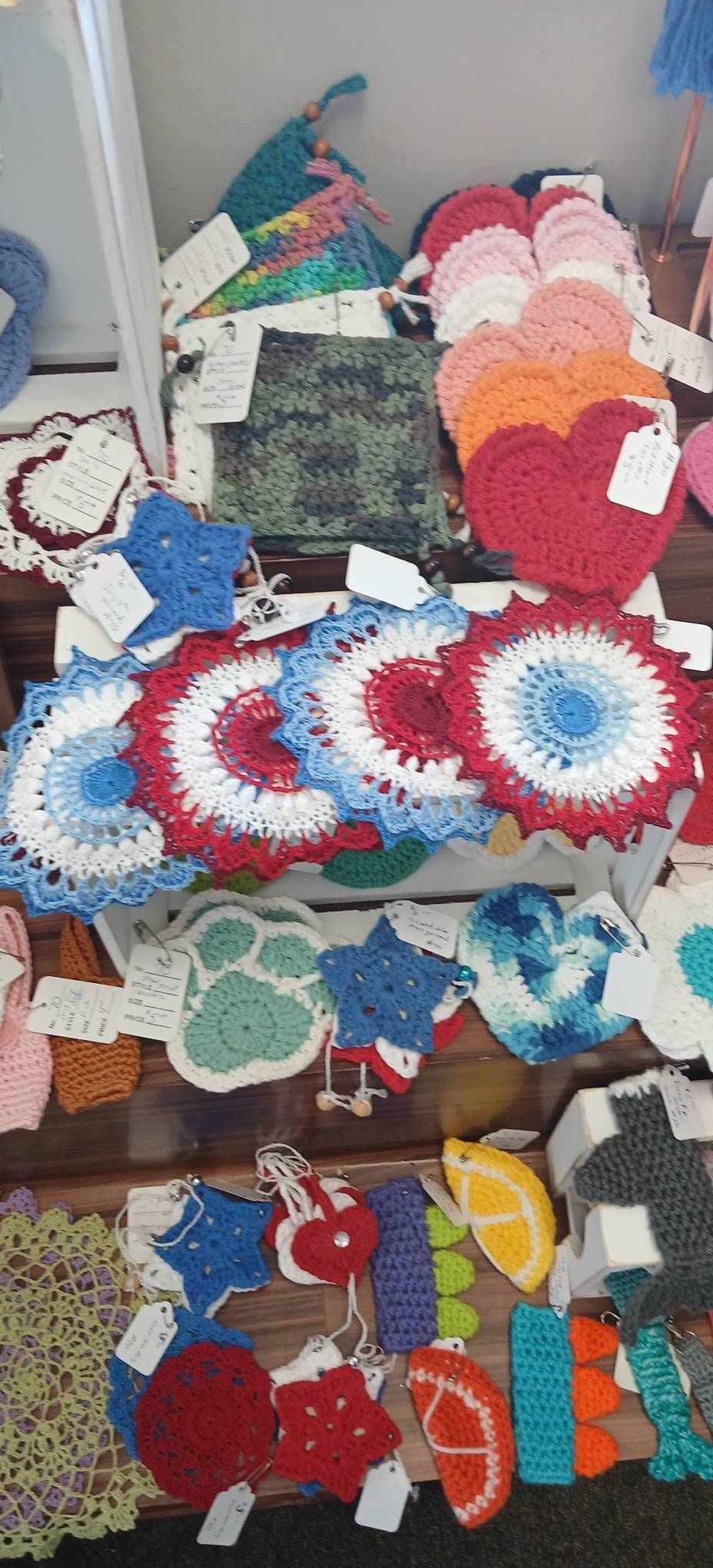 Assorted colorful crocheted doilies and handmade cloth items displayed on a shelf and surface