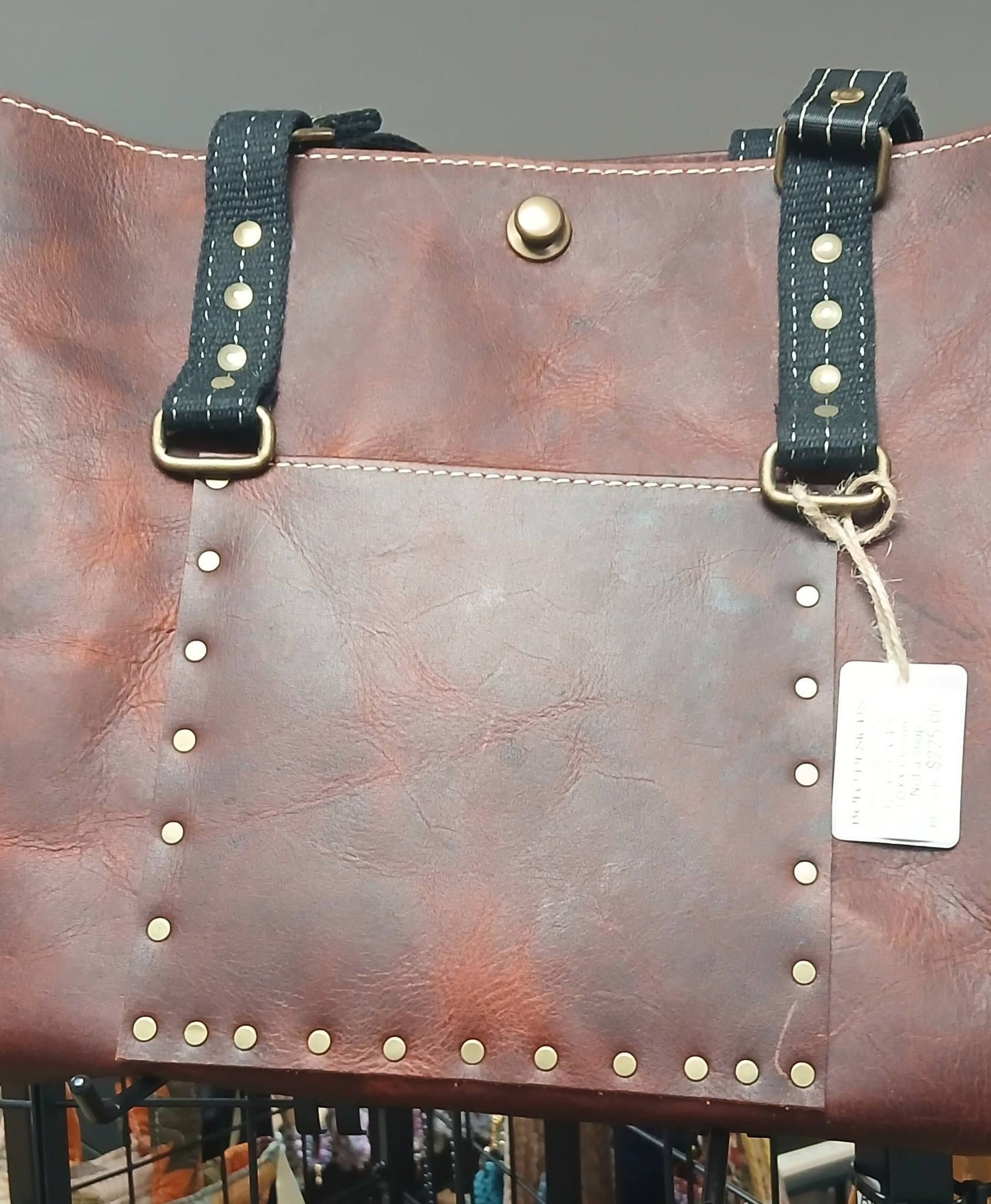 Brown leather handbag with black studded straps and a hanging price tag
