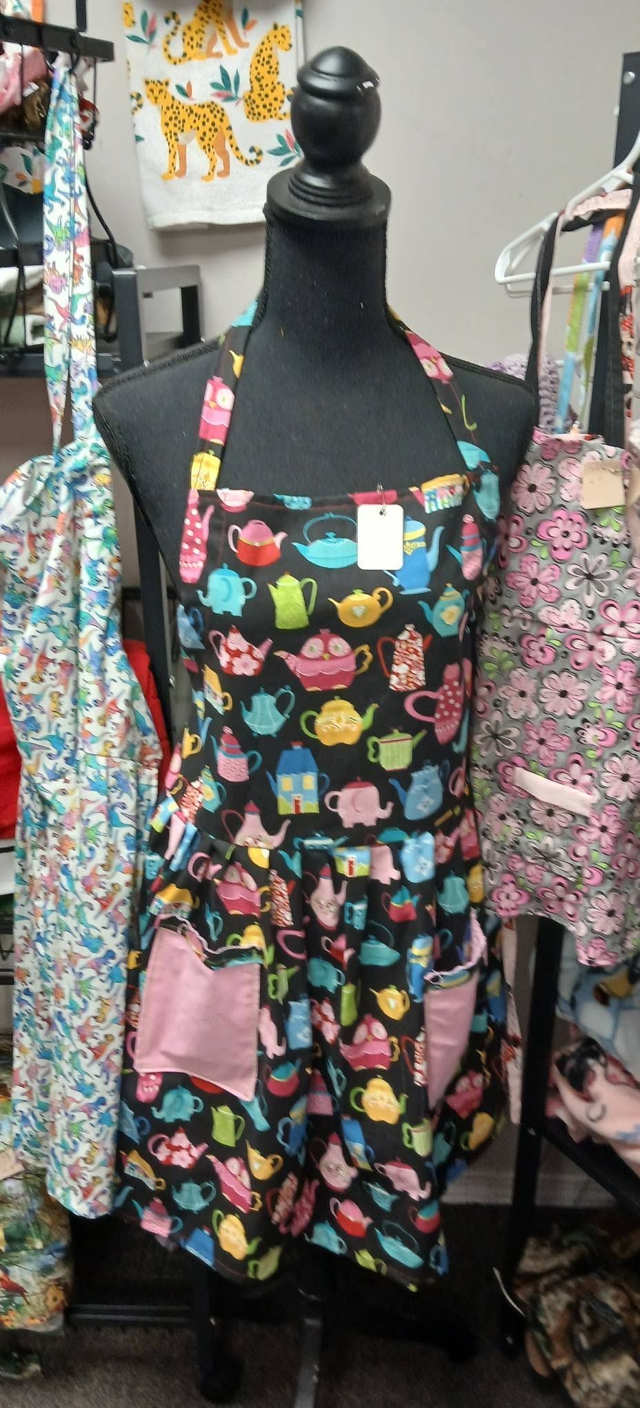 Black dress form displaying a colorful heart-patterned apron with floral sleeves in a craft shop.