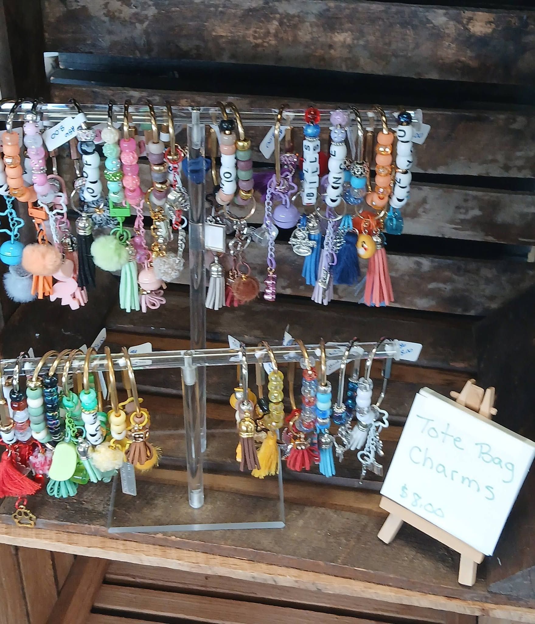 Display of colorful beaded keychains and tassel charms on a wooden shelf, with a small price sign.