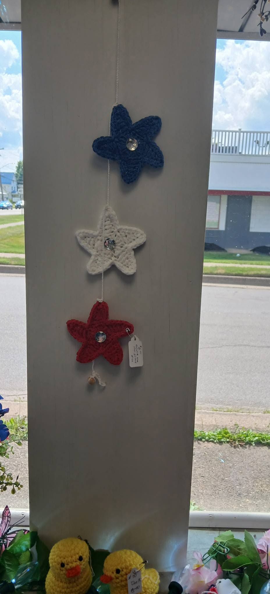 Three hanging flower ornaments in blue, white, and red on a window column