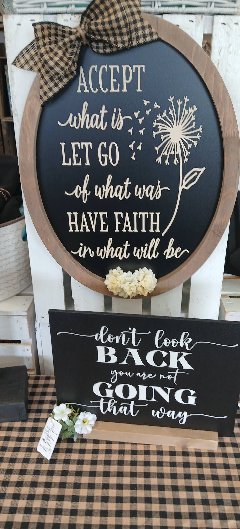 Decorative fall signs with white lettering on a blue round plaque and black hanging board over plaid fabric.