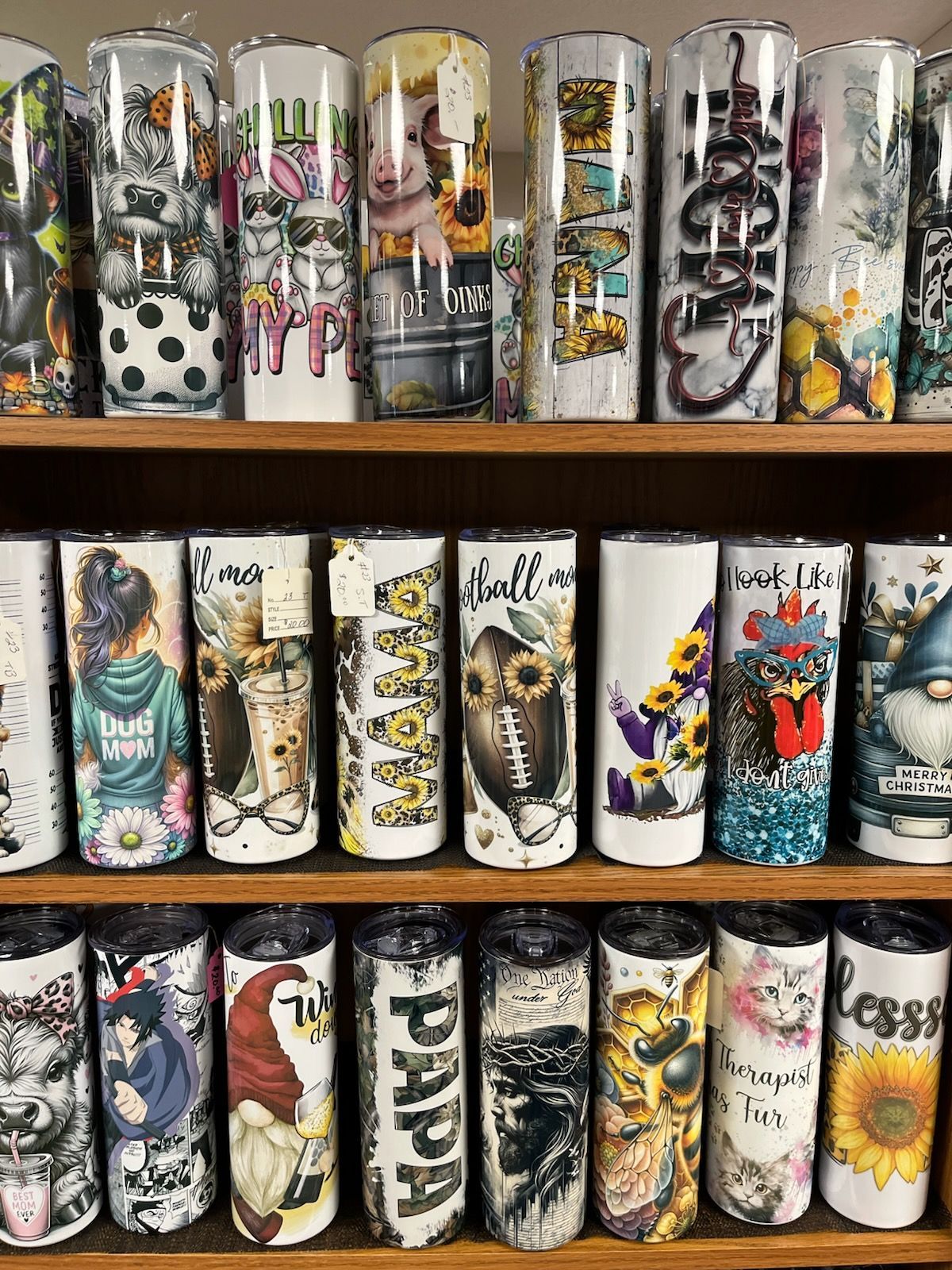 Shelf of colorful decorated tumblers with floral and graphic designs arranged in rows