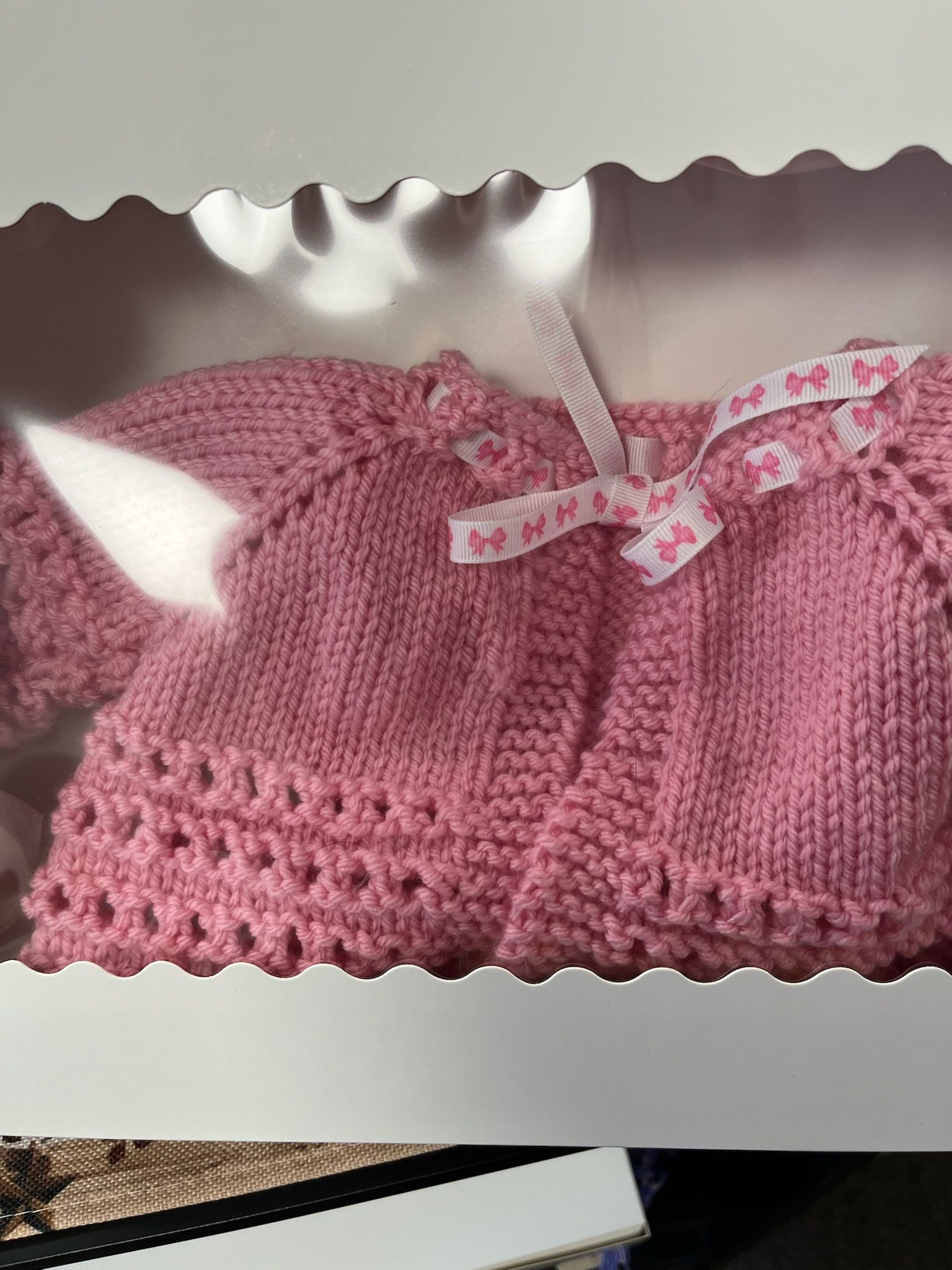 Pink knitted baby sweater with scalloped hem and ribbon bow in a gift box