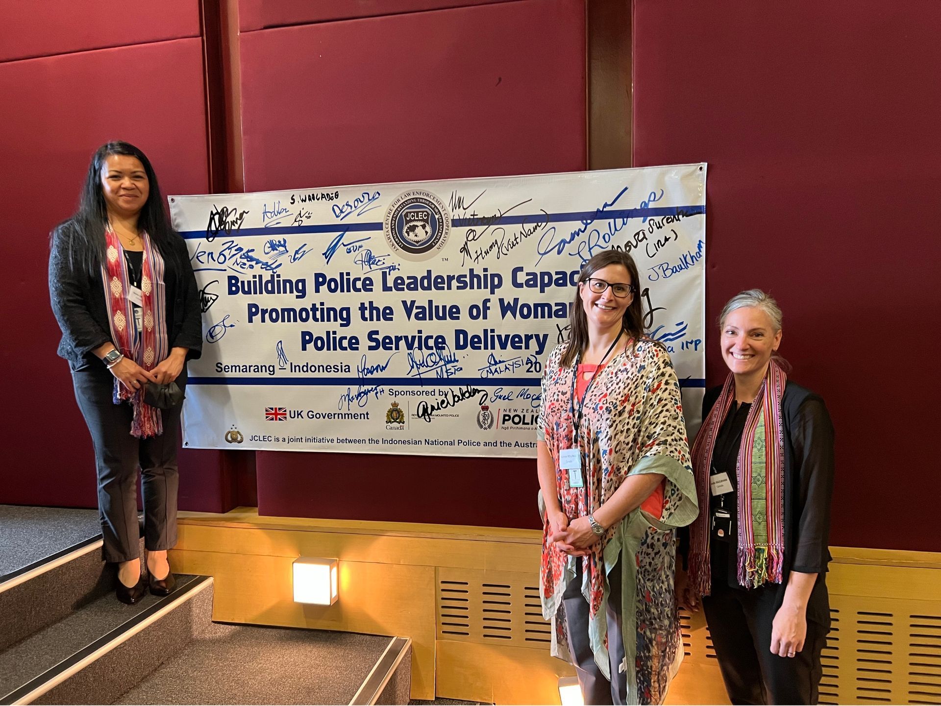 Three women are standing in front of a sign that says building police leadership capacity promoting the value of women police service delivery.