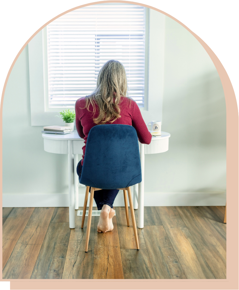 A woman is sitting at a desk in front of a window.