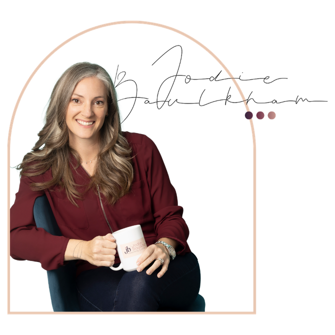 Jodie is sitting in a chair holding a mug and smiling.