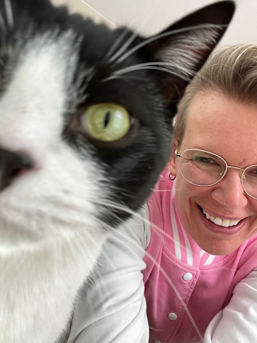 Close-up black-and-white cat beside a smiling person in a pink shirt and glasses