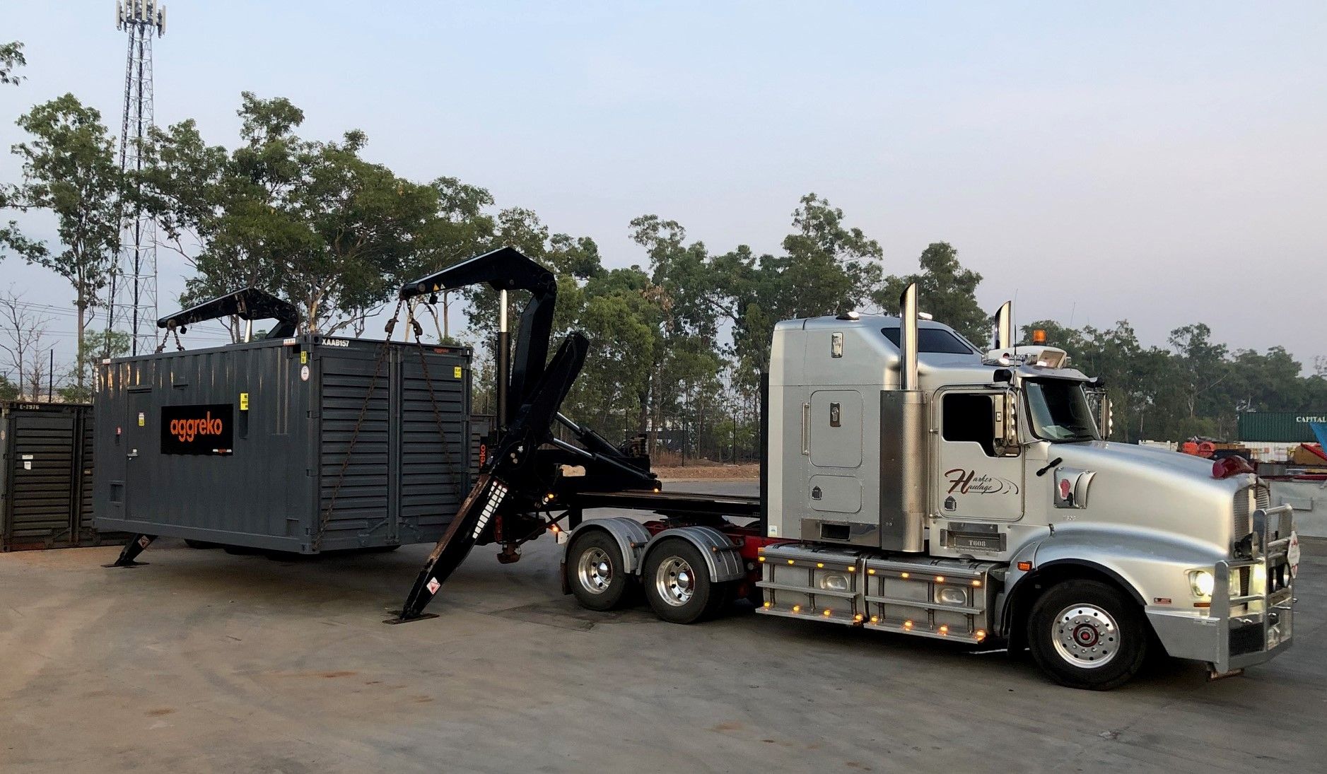 Silver semi-truck towing a large, dark-gray container with attached black support arms, outdoors. — Harker Haulage In East Arm, NT