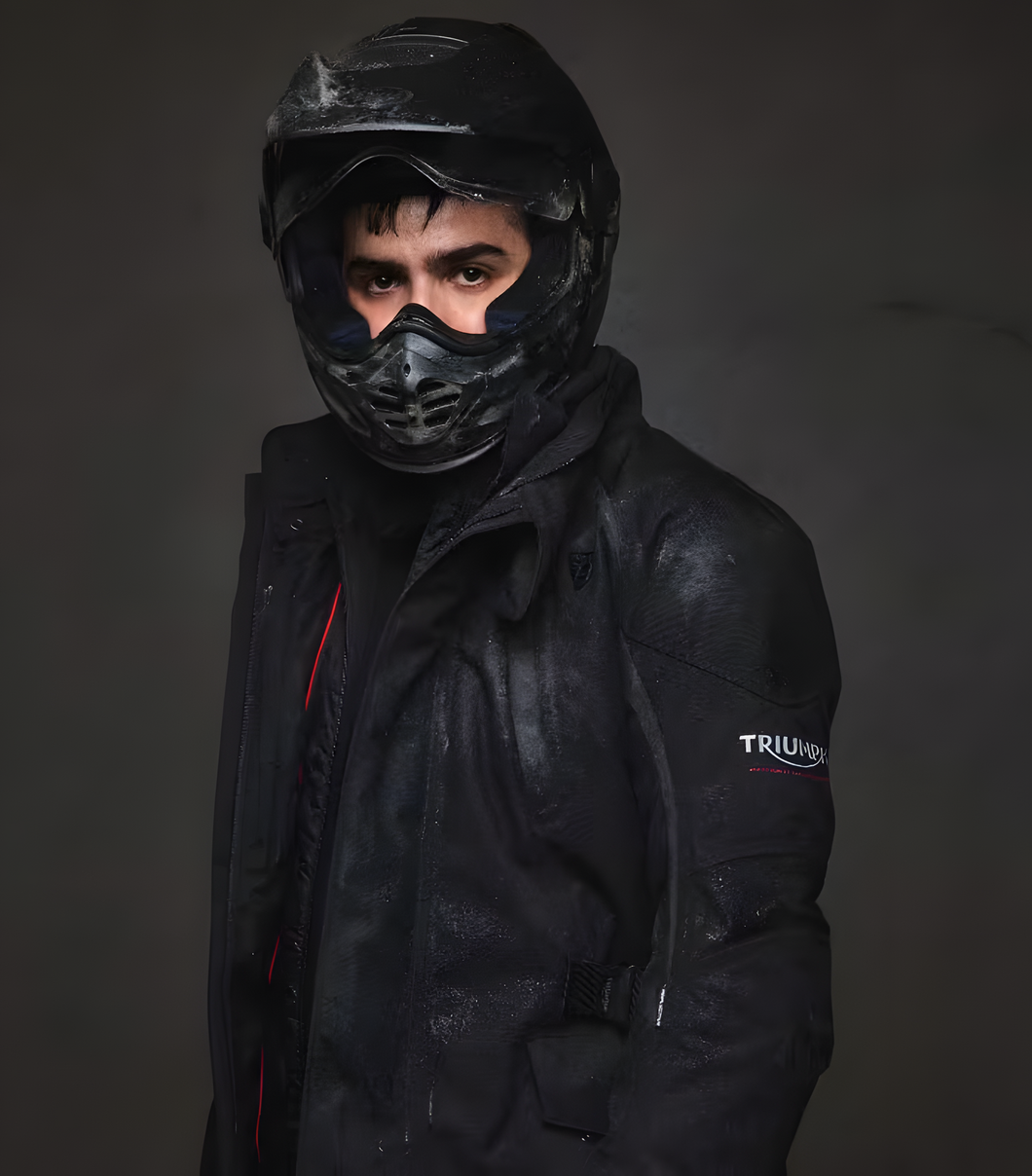 Pessoa com capacete e jaqueta de motociclista pretos contra um fundo escuro.
