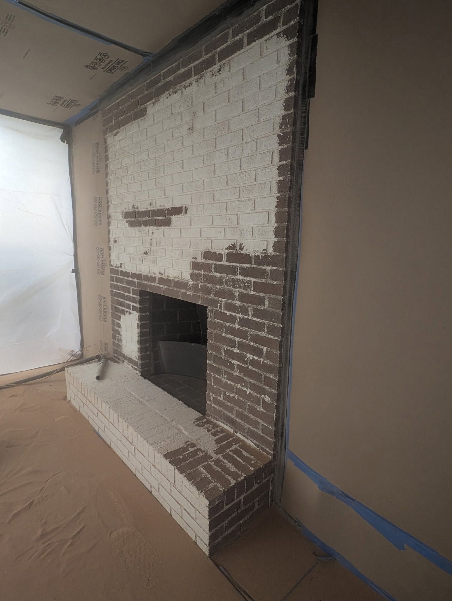 Partially painted brick fireplace in a room under renovation, with protective paper on the floor.