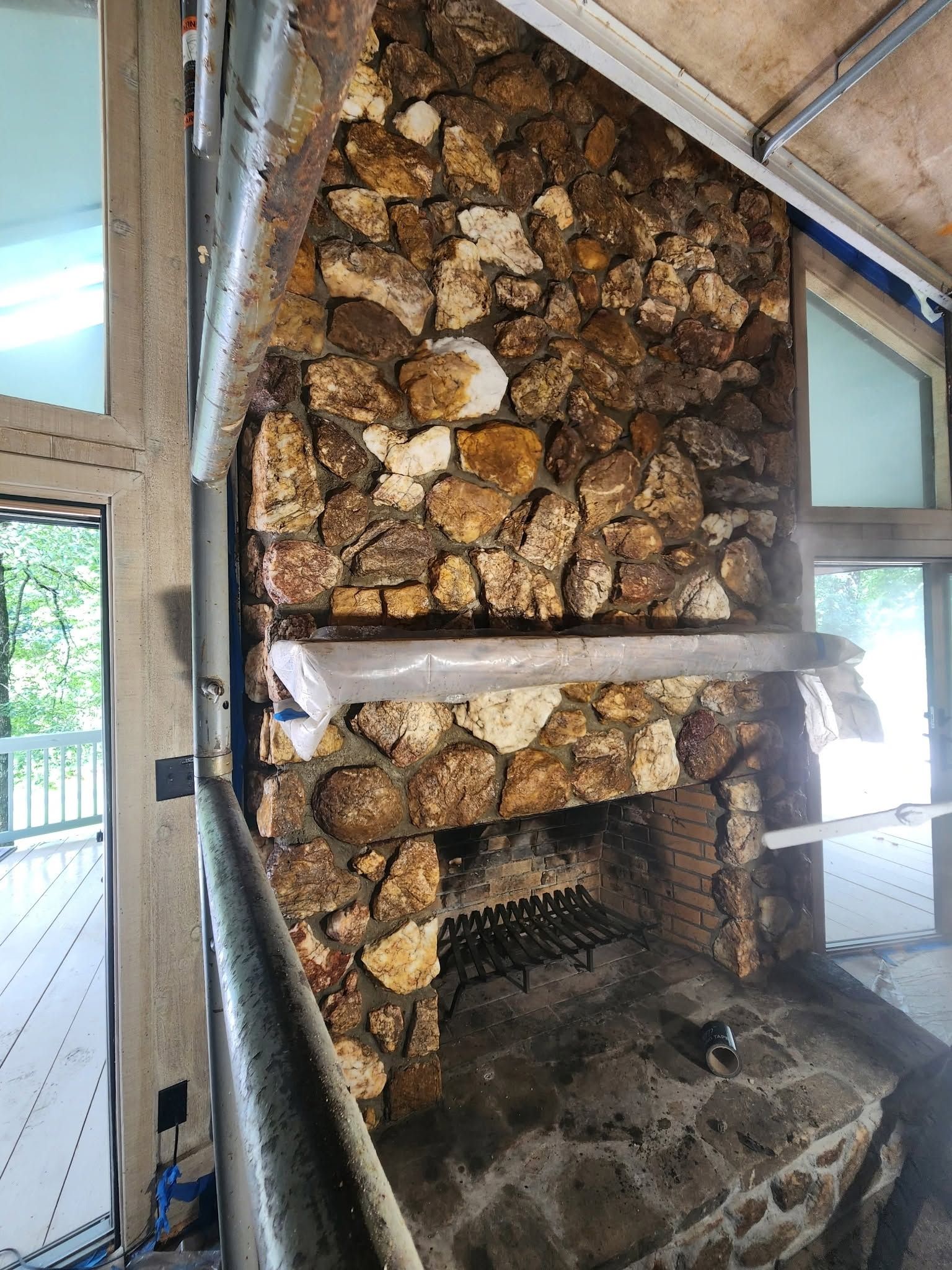 Stone fireplace with a rustic stacked-rock chimney and wooden mantel inside a bright room