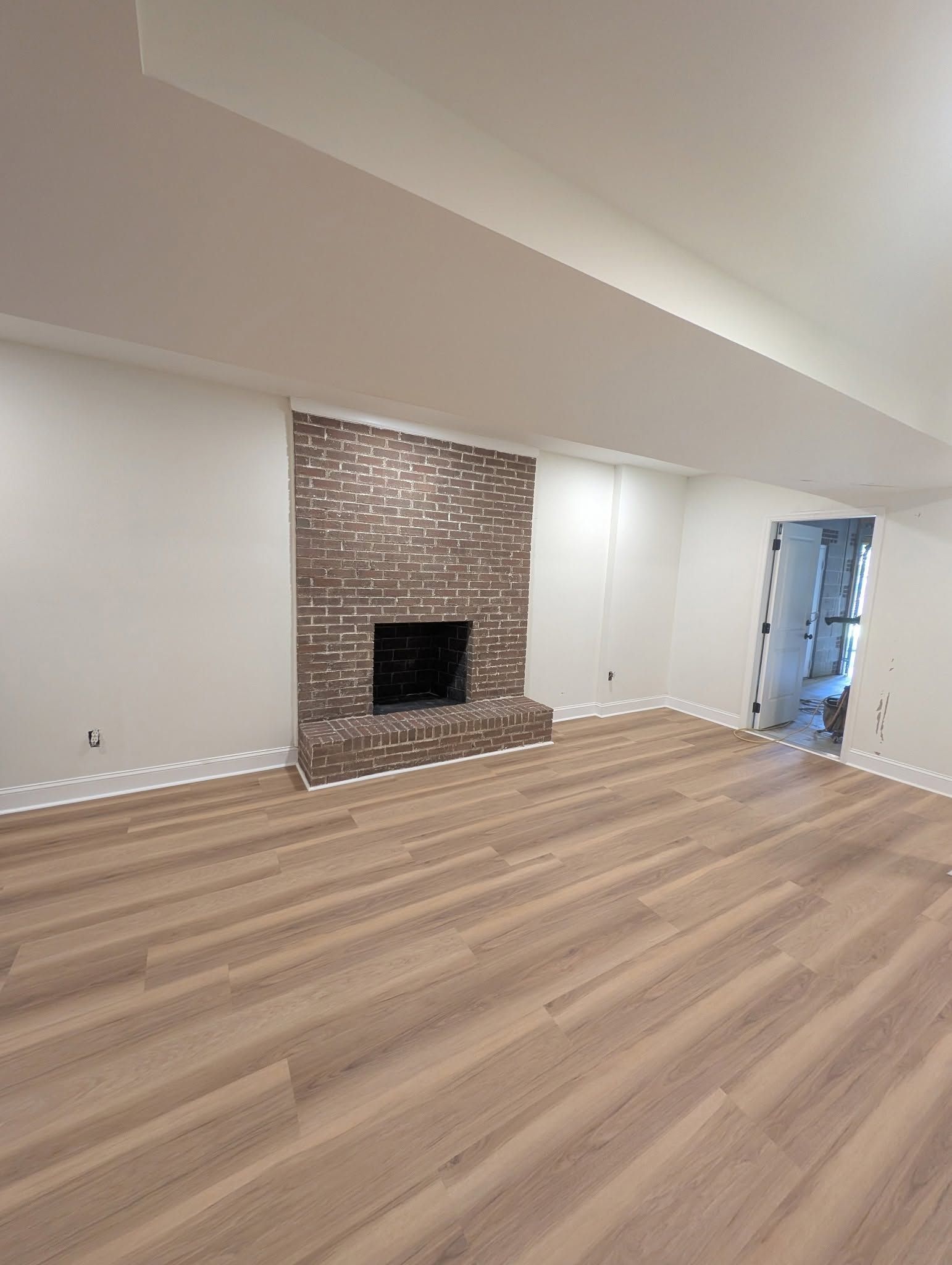 Empty living room with wood floors and a brick fireplace against white walls.