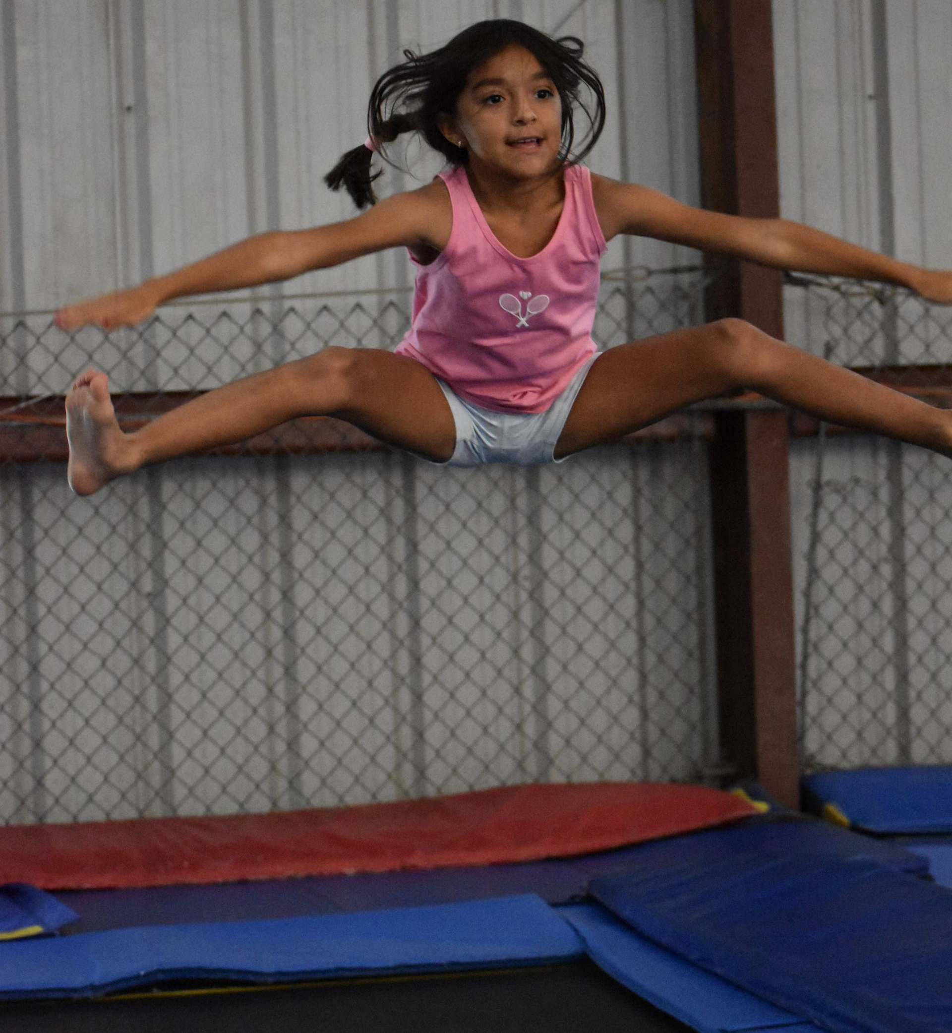 Girl doing a handstand on a mat with a coach and another girl in a gym.