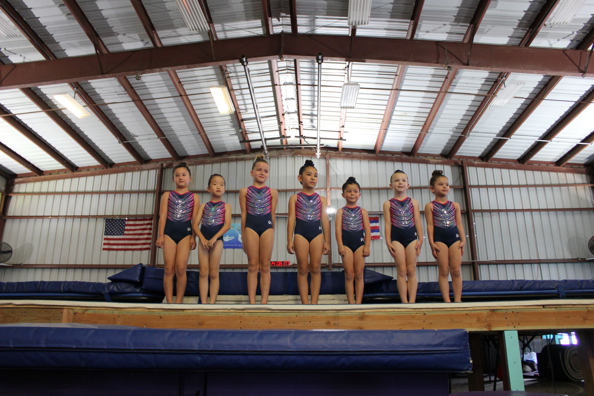 A young girl is sitting on a balance beam in a gym.