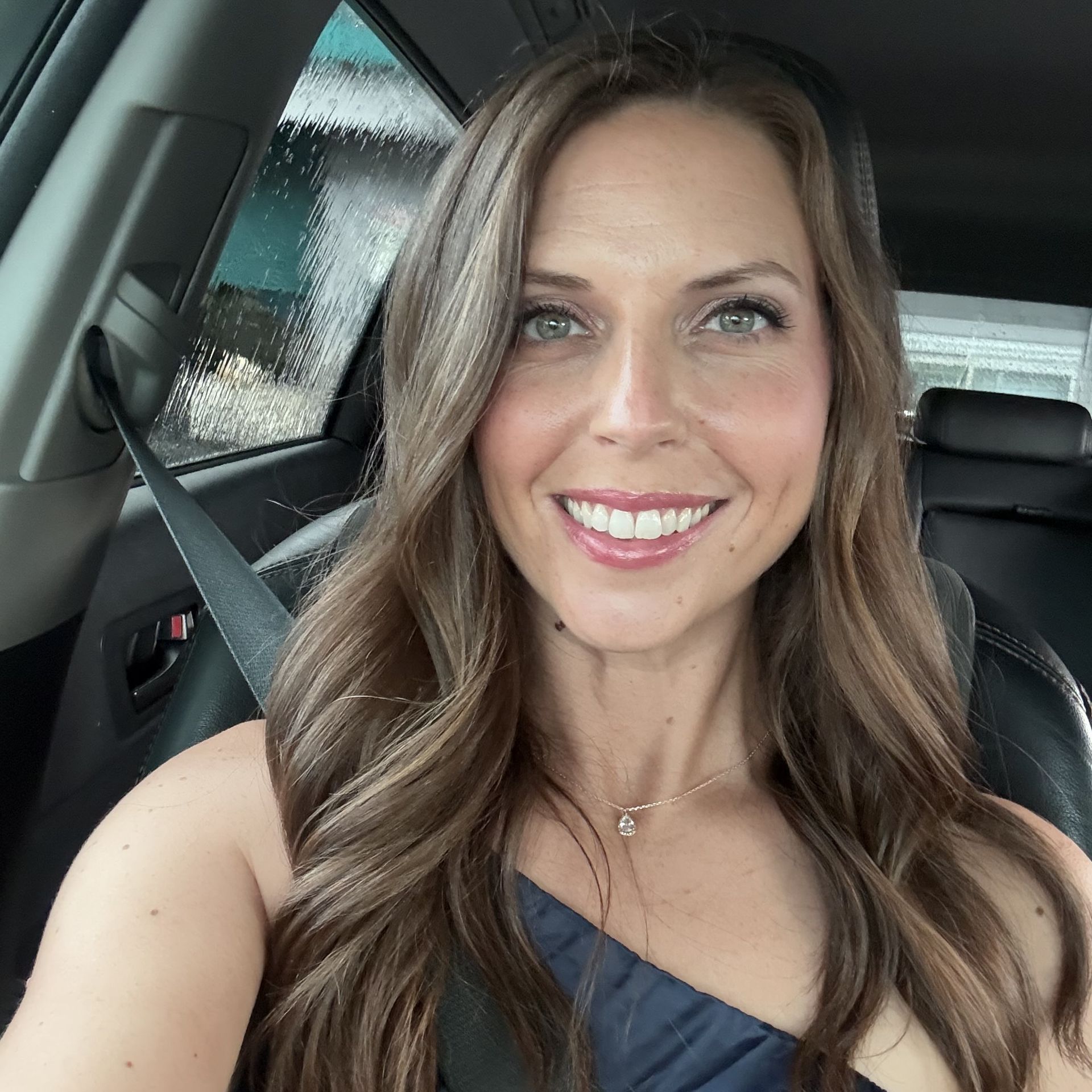 A woman is smiling while sitting in the back seat of a car