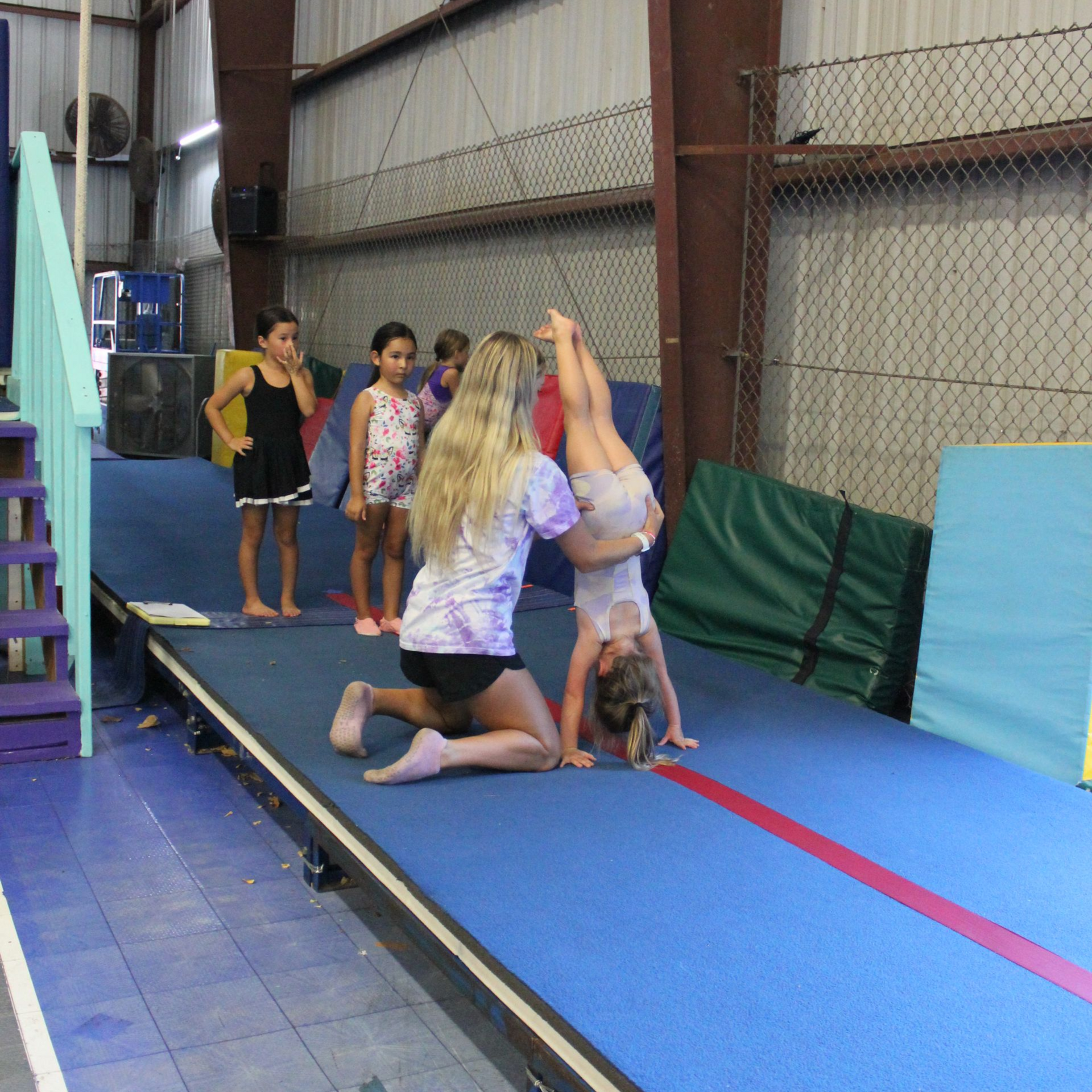 A young girl is sitting on a balance beam in a gym.
