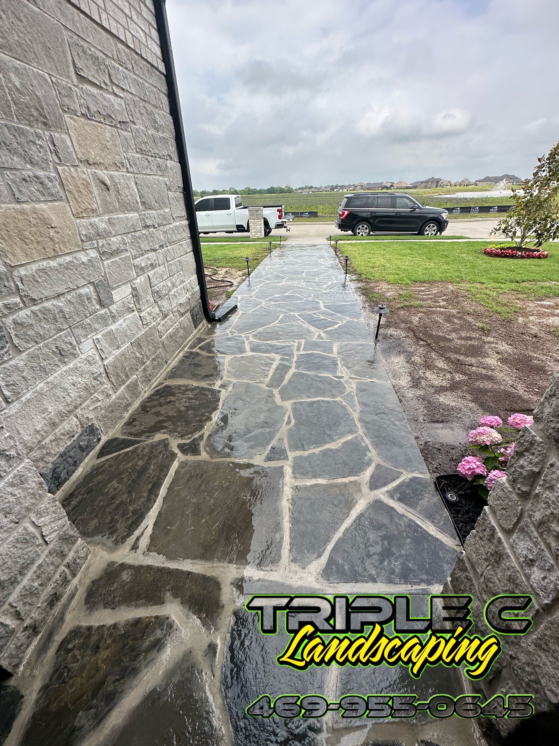 A stone walkway leading to a house with a car parked on the side of it.